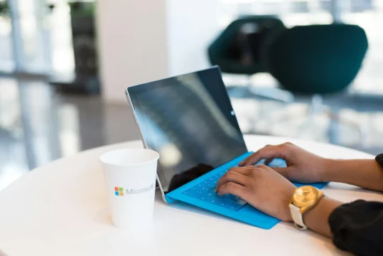 microsoft 365 changes. a woman working on a windows laptop at a desk with a take away coffee cup